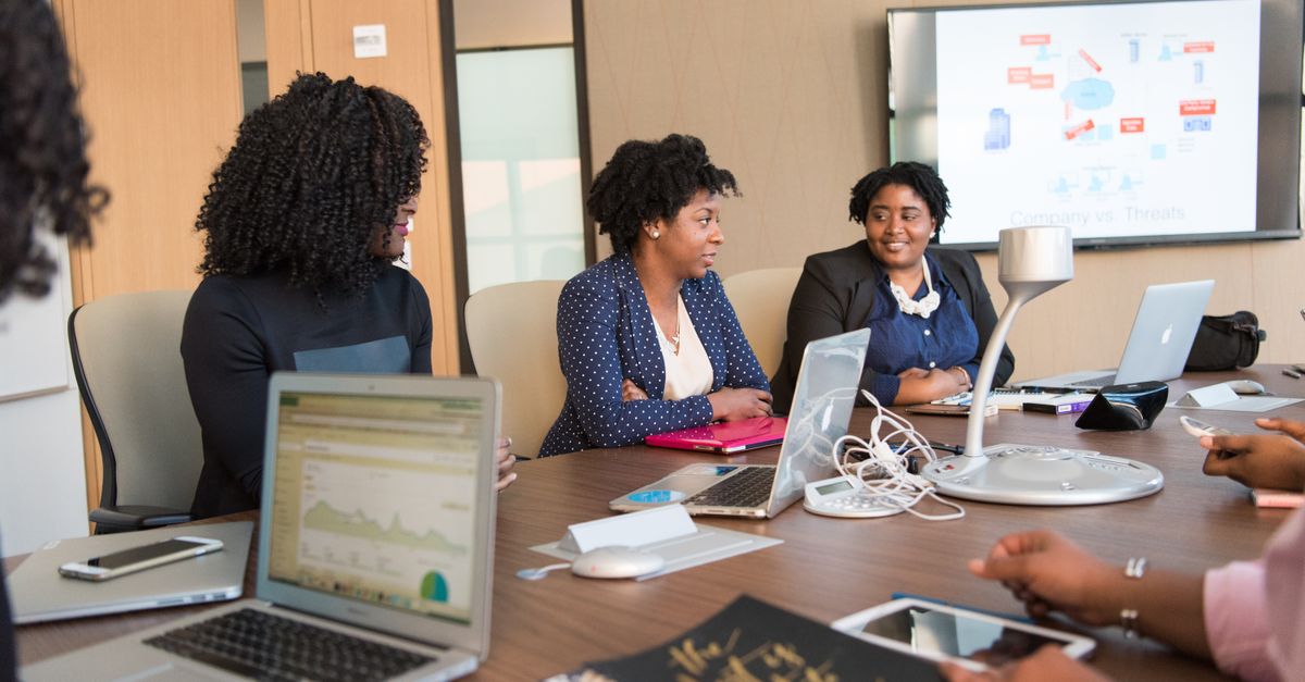 Four diverse women engaged in a business meeting with laptops and presentations in an office.